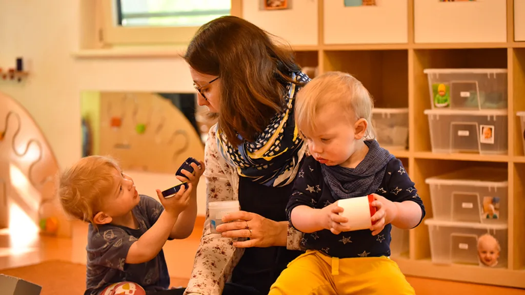 Spielraum der Kinderpropeller-Kita mit einer Erzieherin, die gemeinsam mit zwei Kindern spielt.